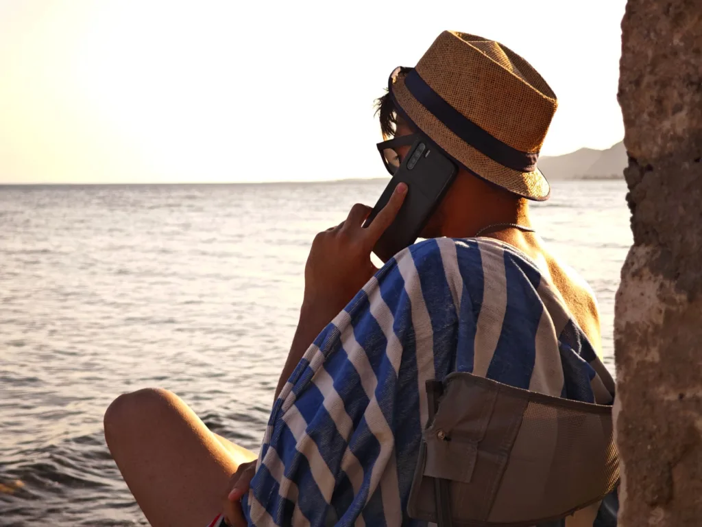 Mężczyzna w kapeluszu rozmawia przez telefon na wybrzeżu